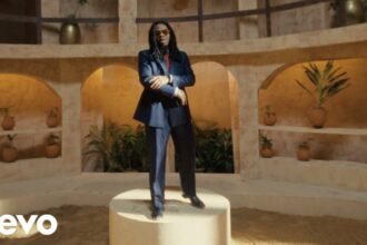 Olamide in the official Burukutu video, wearing a bright outfit and standing against a city backdrop.
