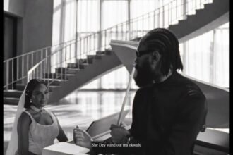 Phyno standing in a softly lit studio, wearing a casual shirt, singing into a microphone while a camera crew records the "Beautiful" music video.