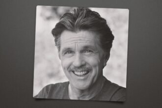 Tom Skerritt wearing a rugged jacket, standing on a film set with a serious expression.
