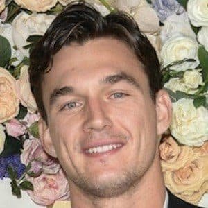 Tyler Cameron, 33-year-old reality TV star and model, standing in a suit smiling at a red carpet event.