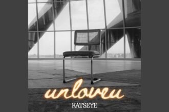 KATSEYE singing Unloveu on stage, wearing a casual shirt, holding a microphone close to his mouth