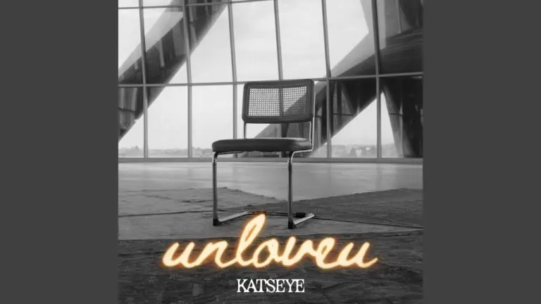 KATSEYE singing Unloveu on stage, wearing a casual shirt, holding a microphone close to his mouth