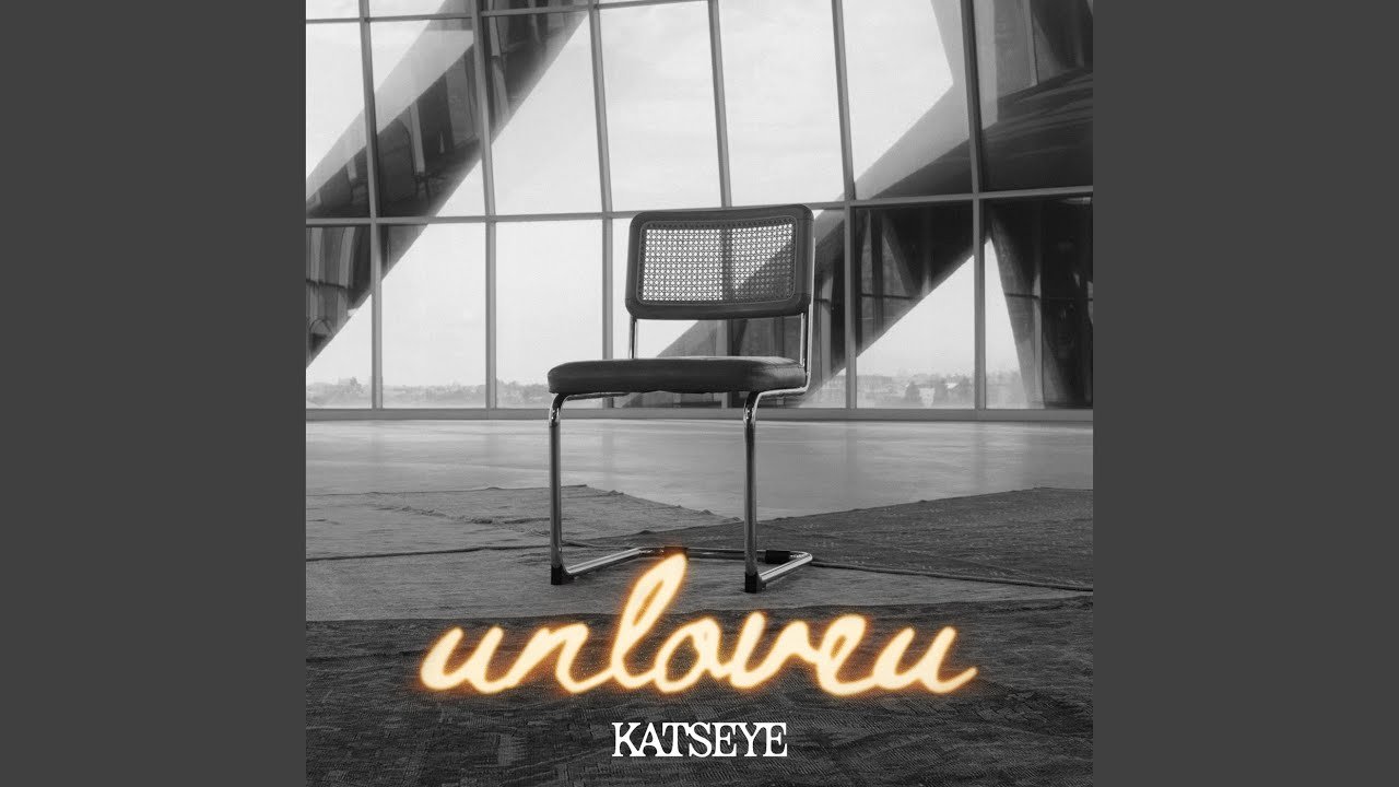 KATSEYE singing Unloveu on stage, wearing a casual shirt, holding a microphone close to his mouth
